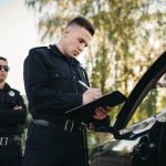 Male police officers in uniform check vehicle on the road with expired tags